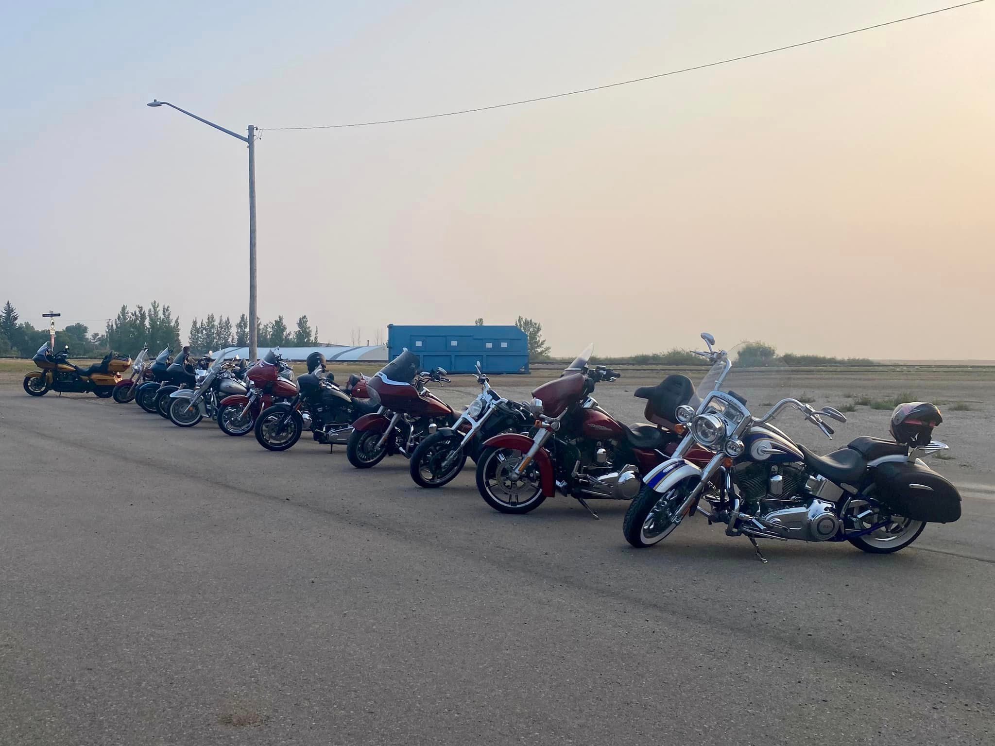 Row of Harley-Davidson bikes lined up on a smoky prairie road at sunset