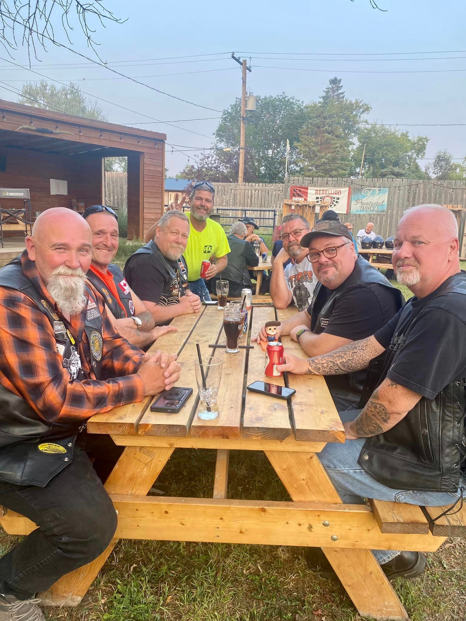 Members in HOG vests relaxing at outdoor picnic tables with Rebellion Vodka banners