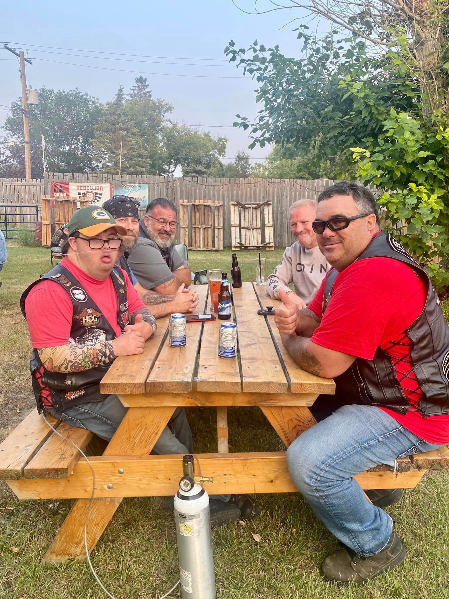 Members in HOG vests at a picnic table with Kokanee beers at an outdoor stop