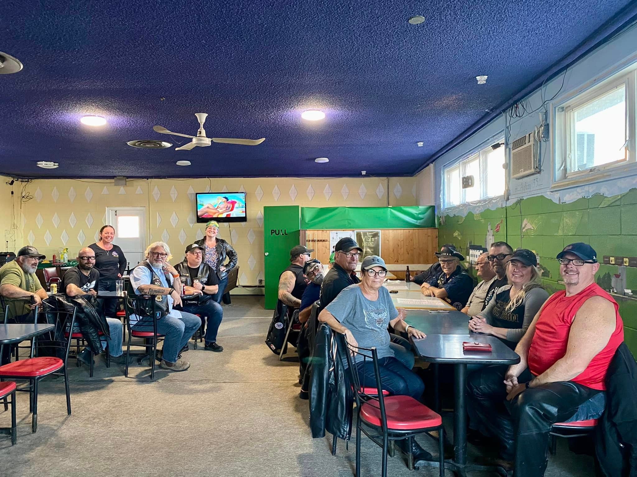 Chapter members gathered inside a small-town bar with a blue ceiling on a ride stop