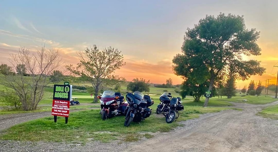 Three bikes parked at a golf course Hole 1 access sign at sunset