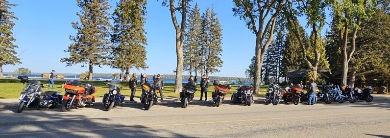 Wide shot of chapter bikes parked lakeside under tall pines at a ride stop