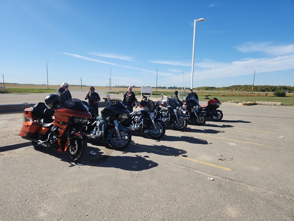 Bikes lined up in a flat prairie parking lot under a wide blue sky at a ride stop