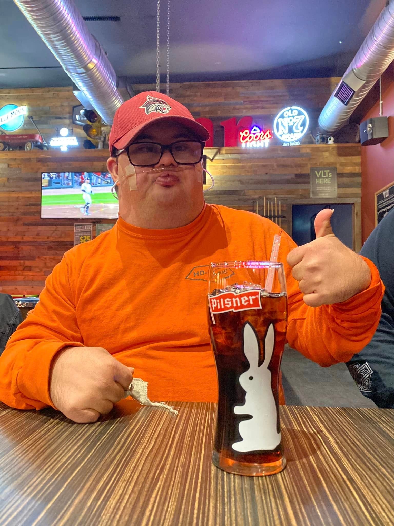 Chapter member in an orange HOG shirt giving a thumbs-up with a Pilsner glass at a ride stop bar