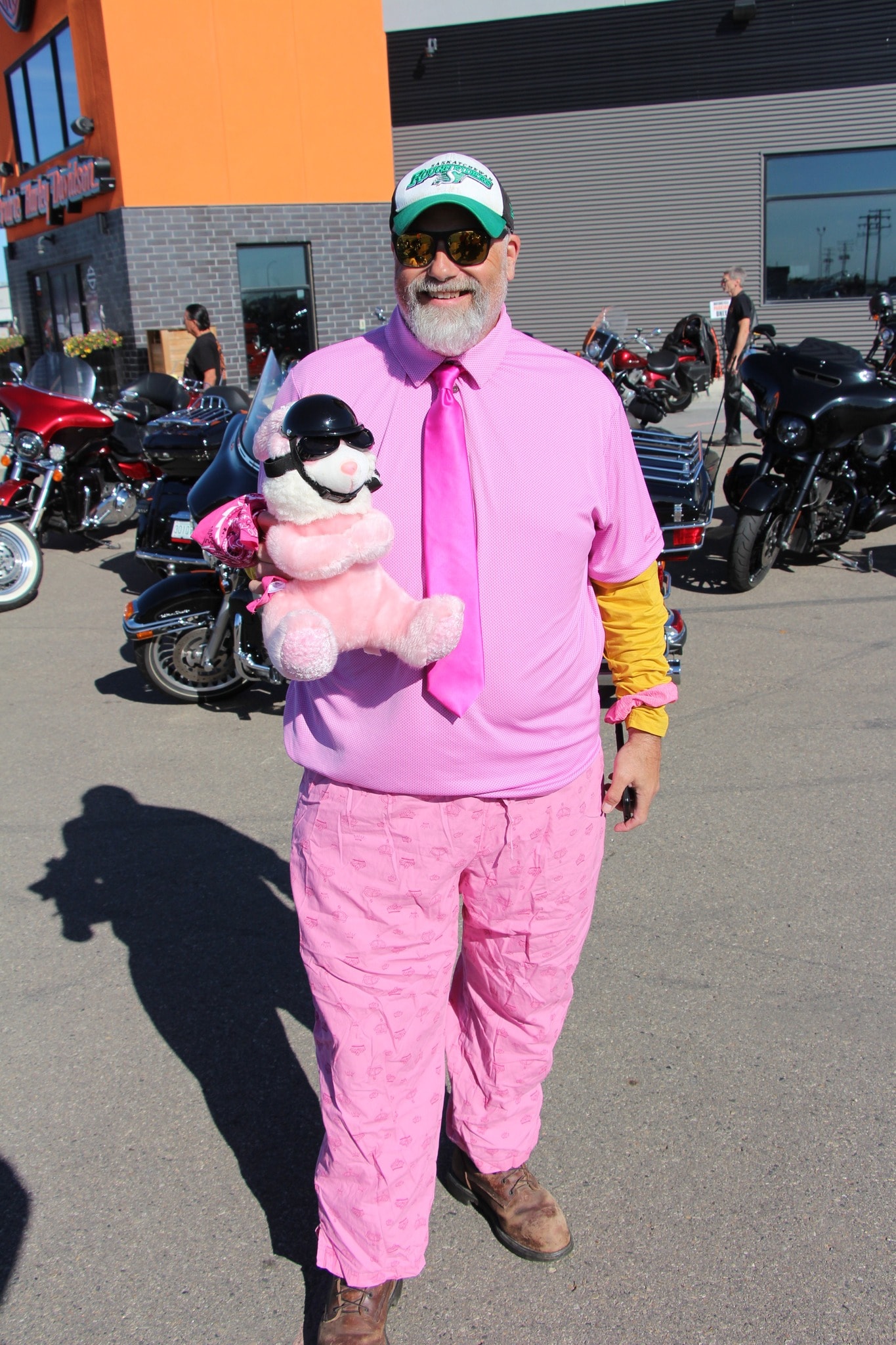 Member in full pink outfit holding a stuffed bear with a motorcycle helmet at the charity ride