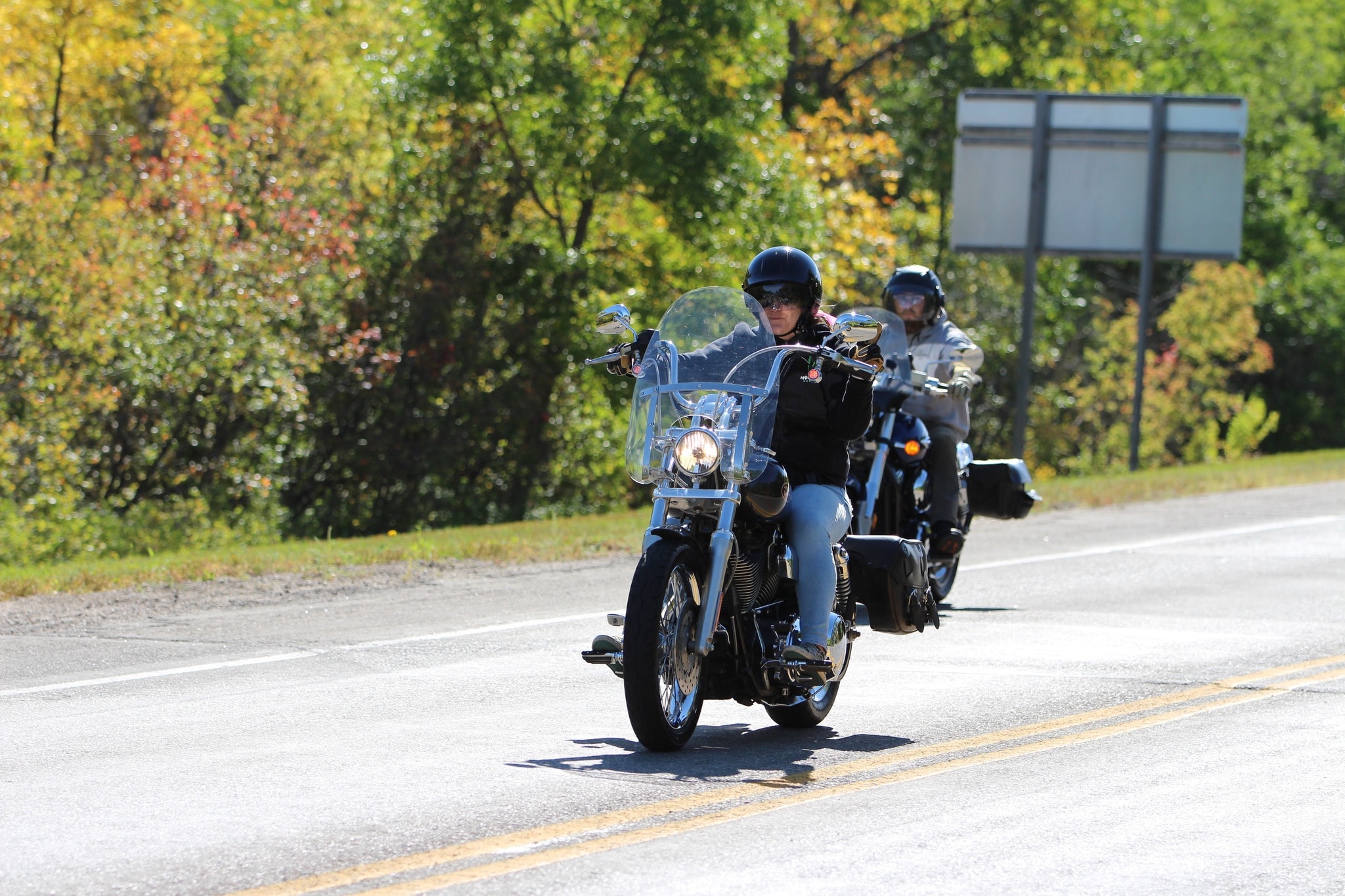 Two riders on Harley-Davidsons coming through autumn foliage on the 2024 Breast Cancer Awareness Ride