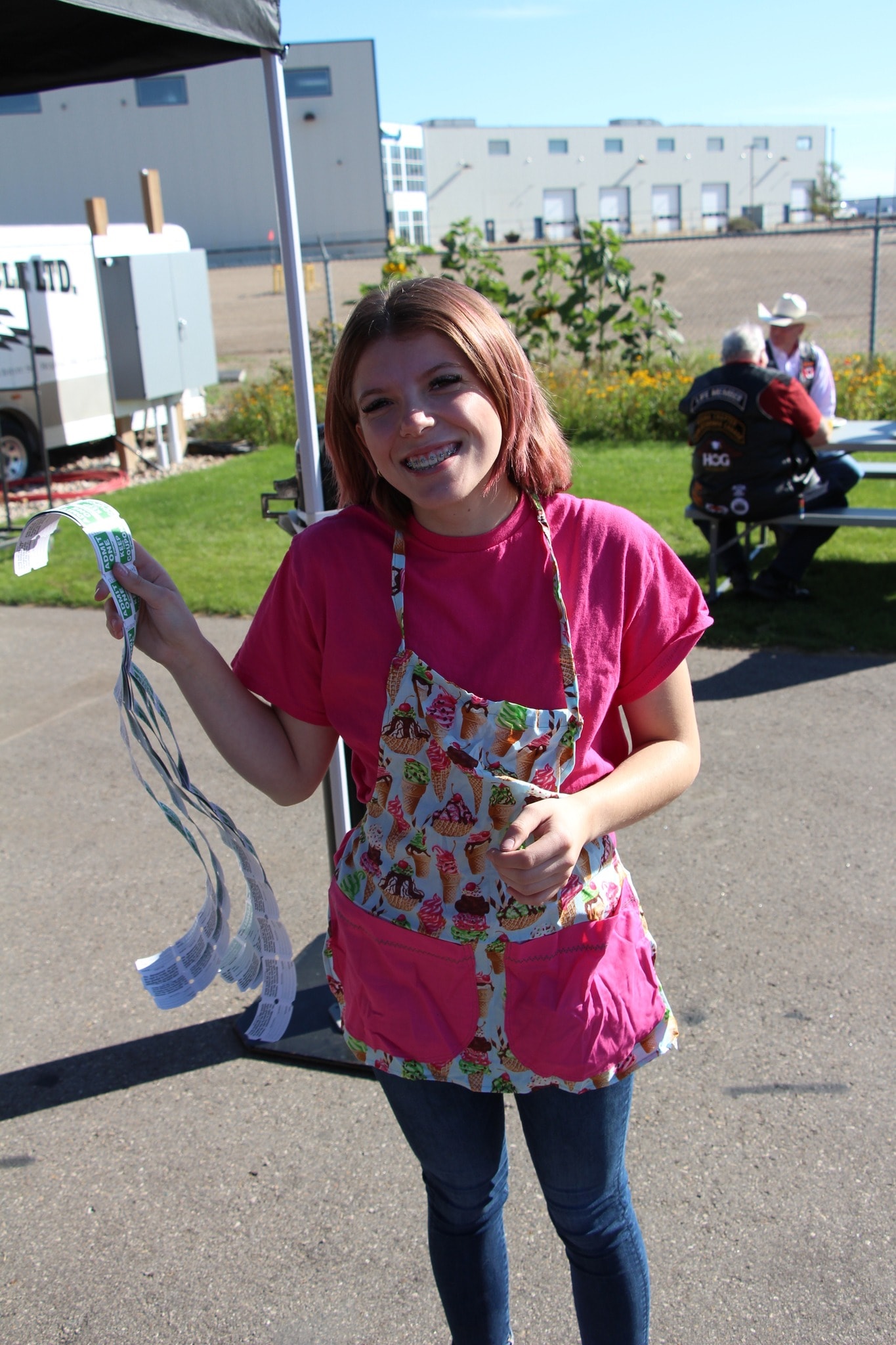 Volunteer in a pink shirt and ice cream apron holding raffle tickets at the charity ride