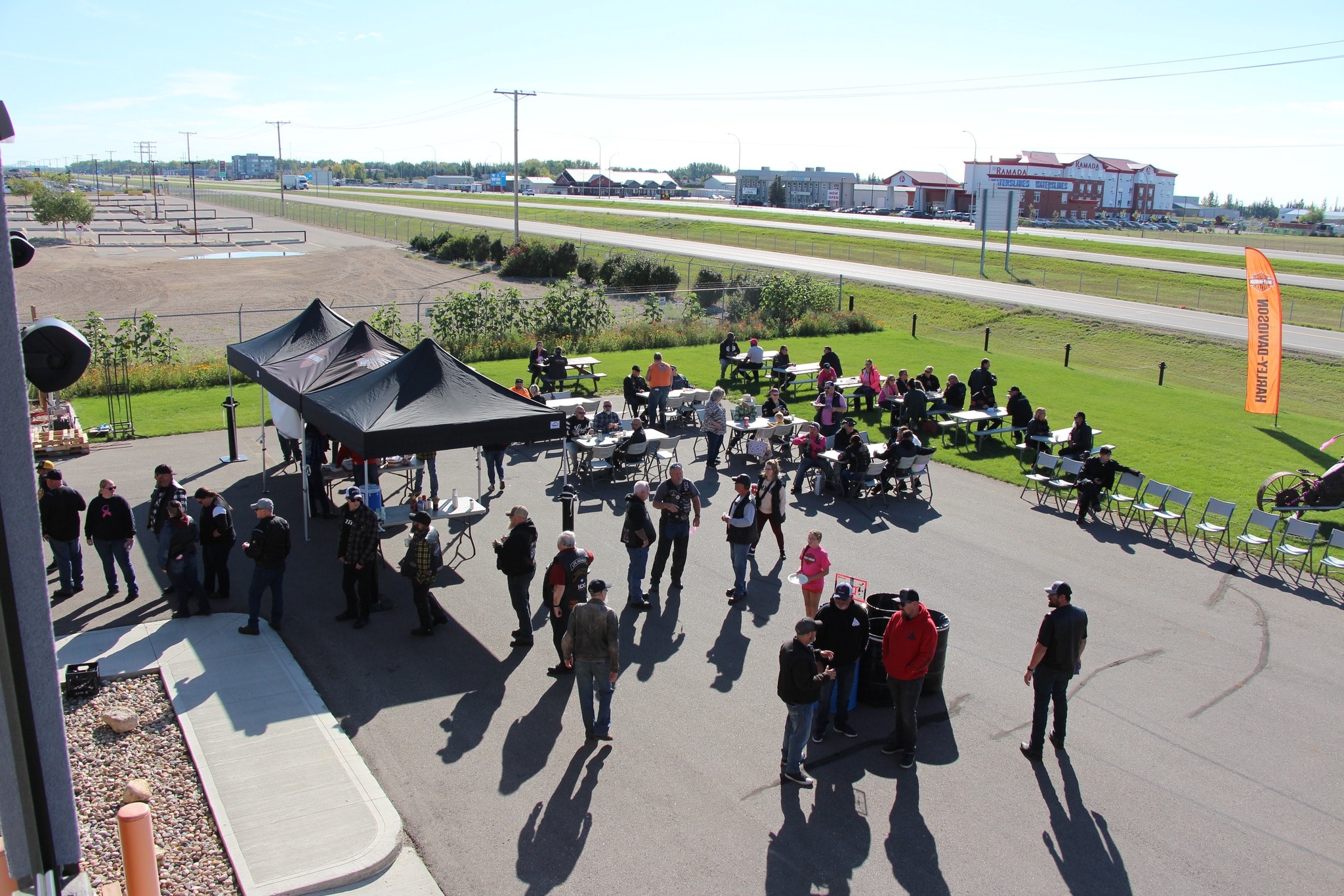 Aerial view of riders gathered under a black tent and at outdoor tables at the 2024 Breast Cancer Awareness Ride at Prairie Harley-Davidson