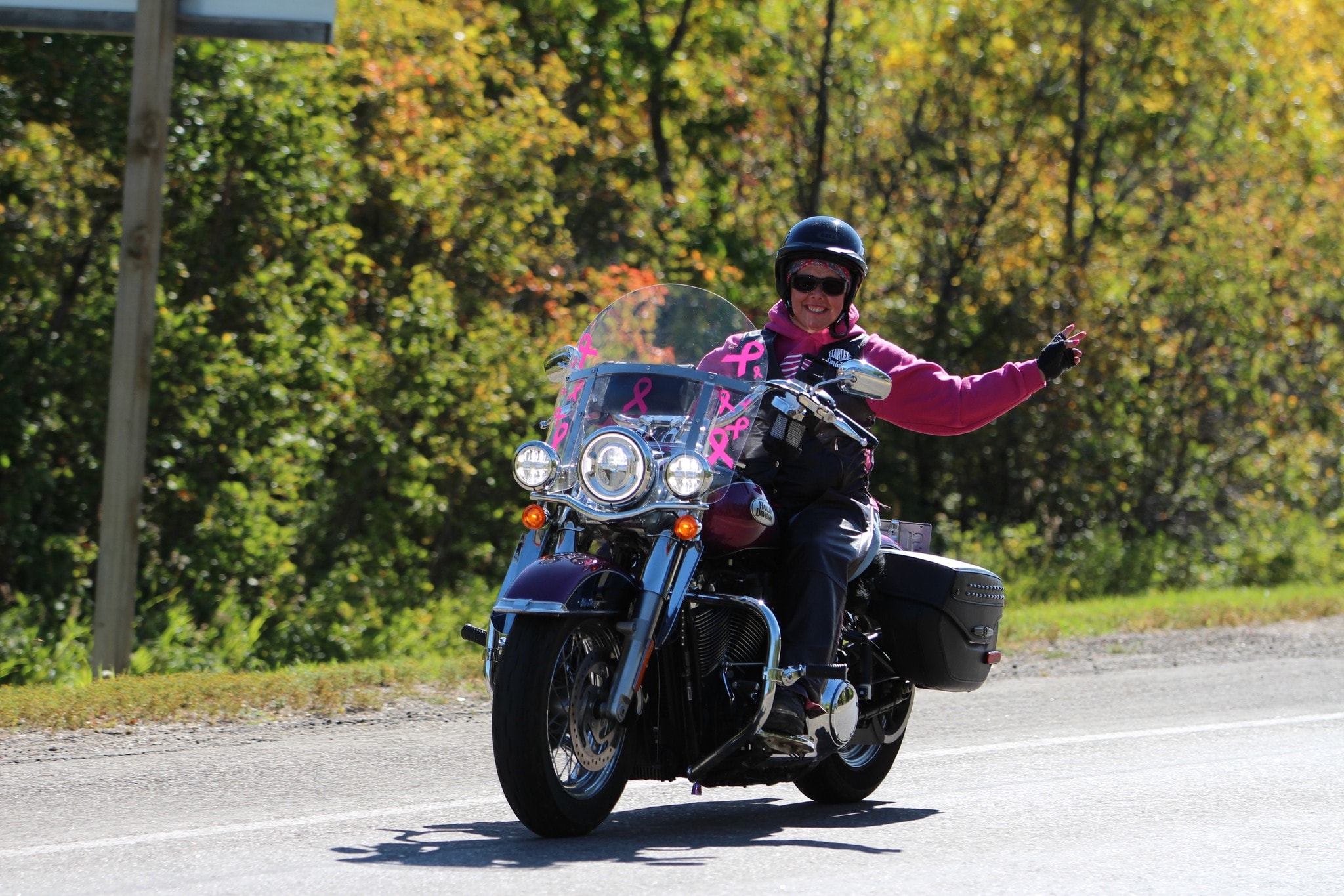 Smiling rider in pink on a pink-ribbon-decorated Harley-Davidson giving a wave on the 2024 Breast Cancer Awareness Ride