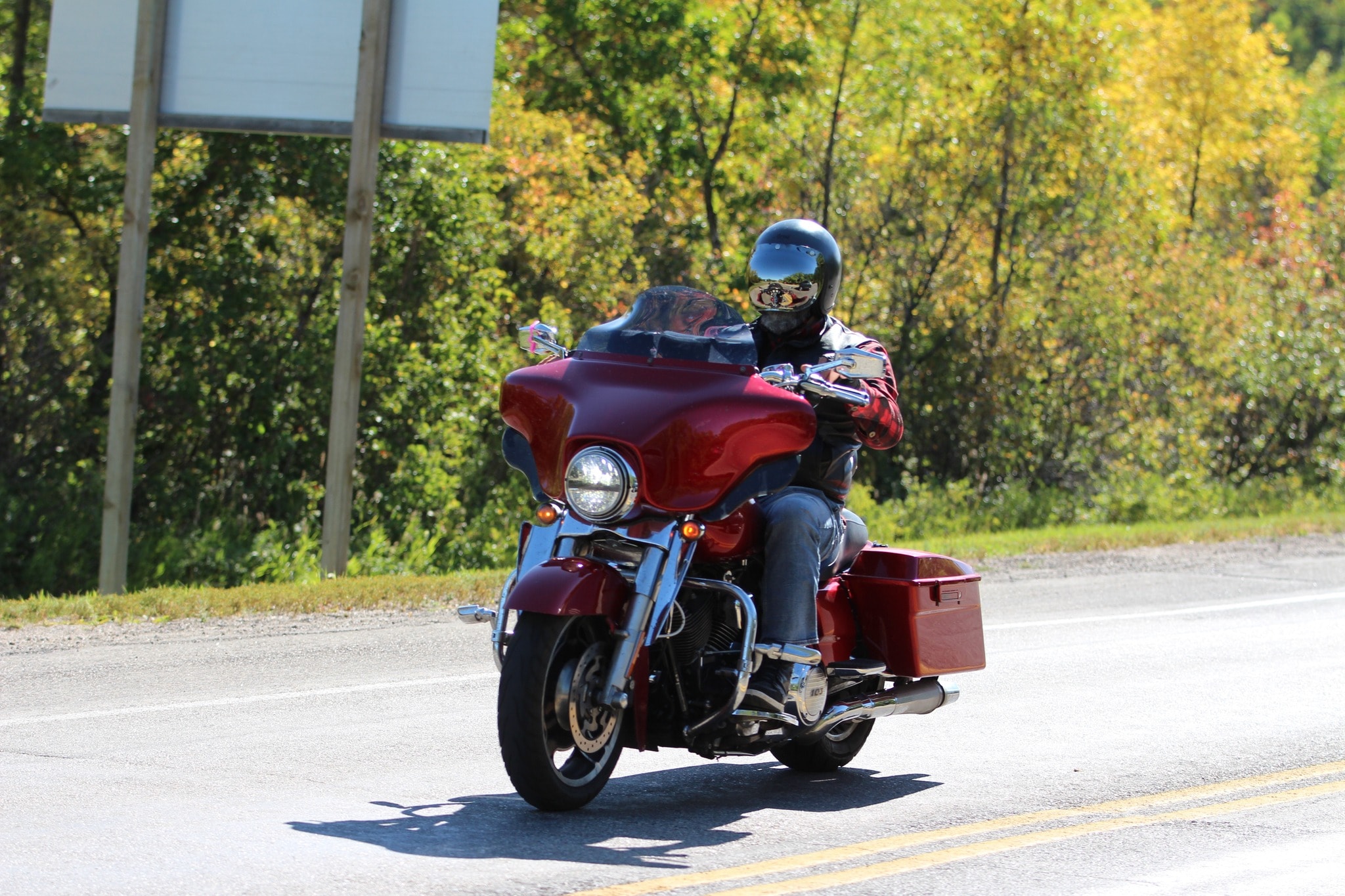 Rider on a red Harley-Davidson touring bike coming through autumn foliage on the 2024 Breast Cancer Awareness Ride