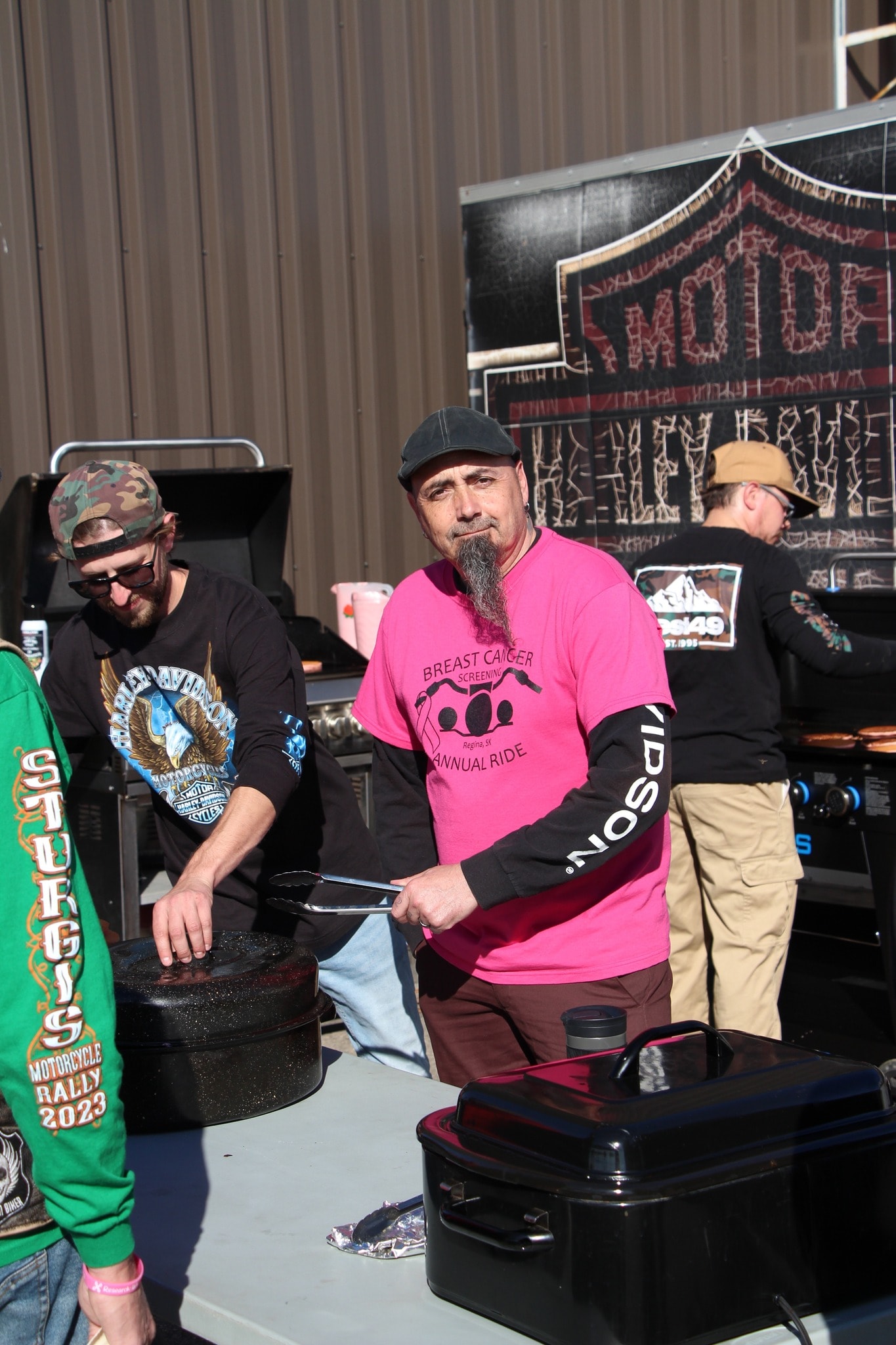 Volunteer in a pink Breast Cancer Screening Annual Ride shirt working the breakfast grill outside Prairie Harley-Davidson