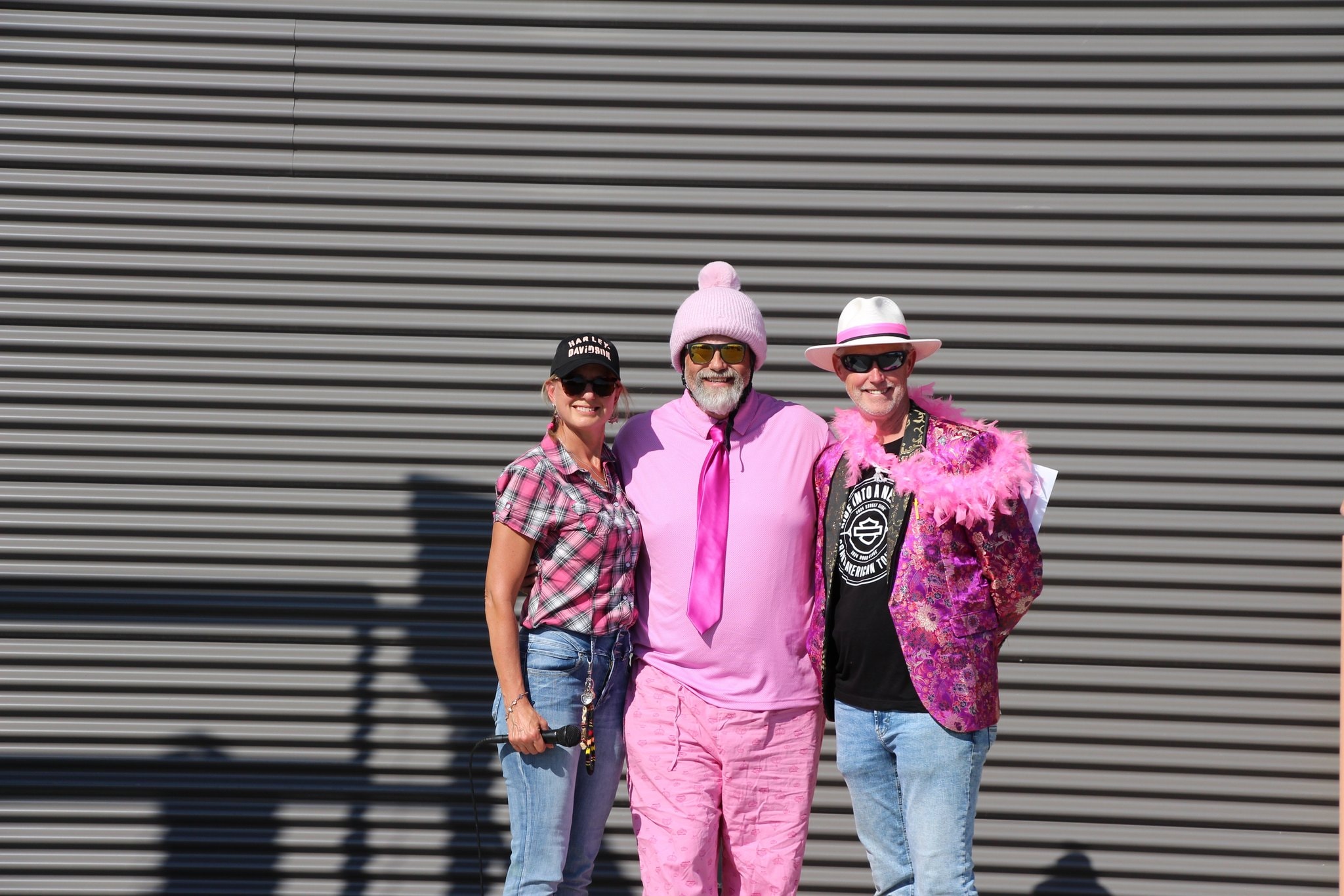 Three members in pink charity ride attire posing outside Prairie Harley-Davidson