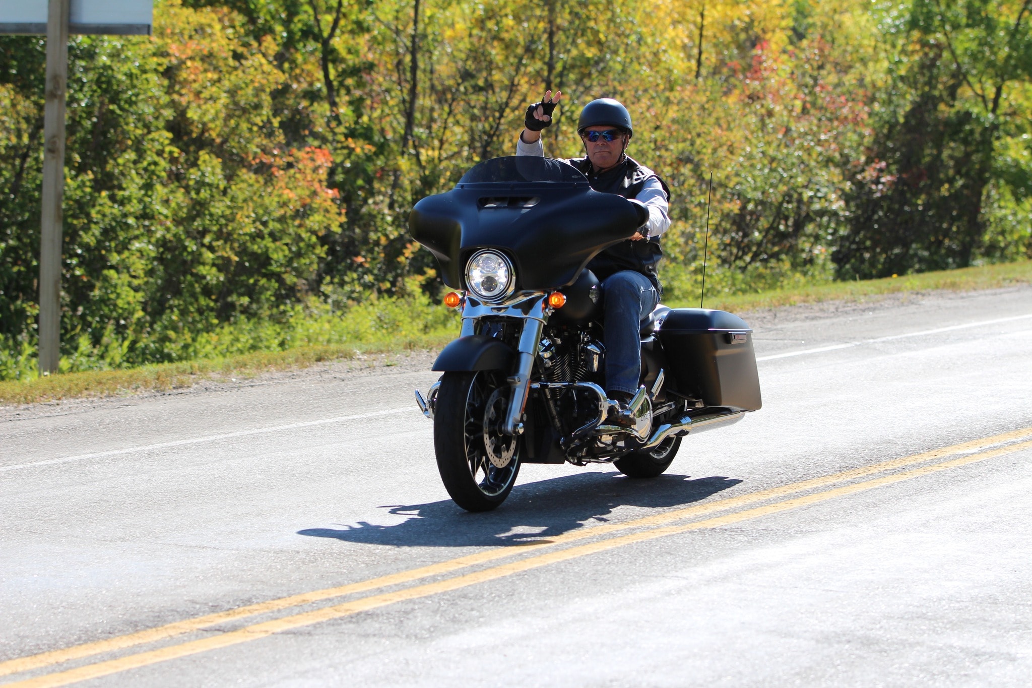 Rider on a black Harley-Davidson giving a wave while riding through autumn foliage on the charity ride
