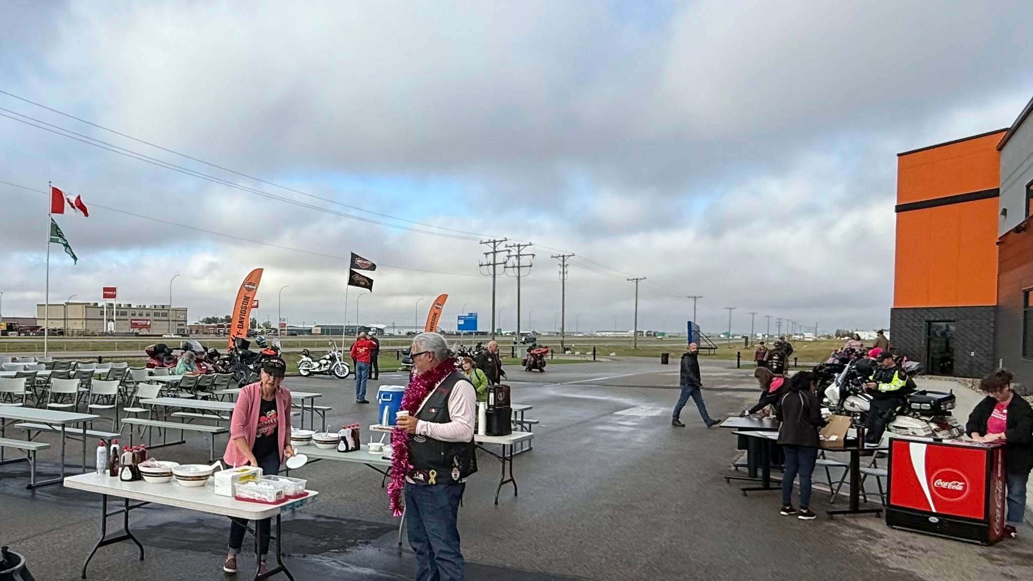 Outdoor breakfast setup at Prairie Harley-Davidson with folding tables, Coca-Cola cooler and Harley-Davidson banners flying at the 2025 Breast Cancer Awareness Ride