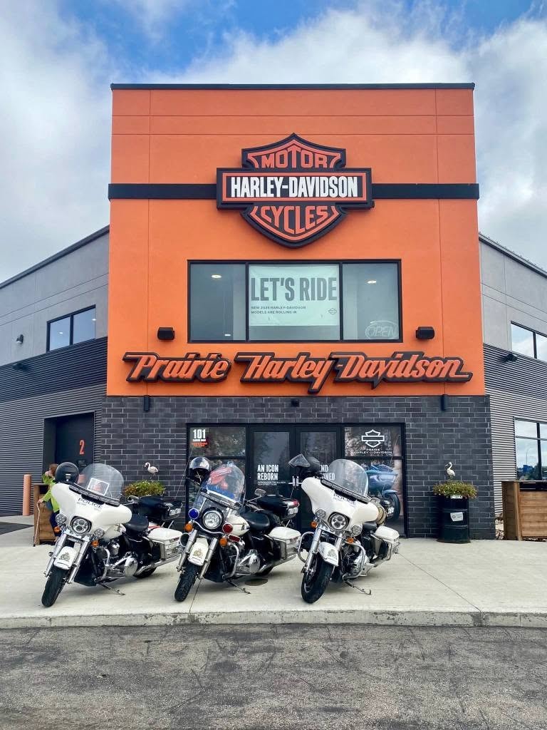 Three police Harley-Davidson motorcycles parked in front of the Prairie Harley-Davidson storefront with the Let's Ride banner at the 2025 Breast Cancer Awareness Ride
