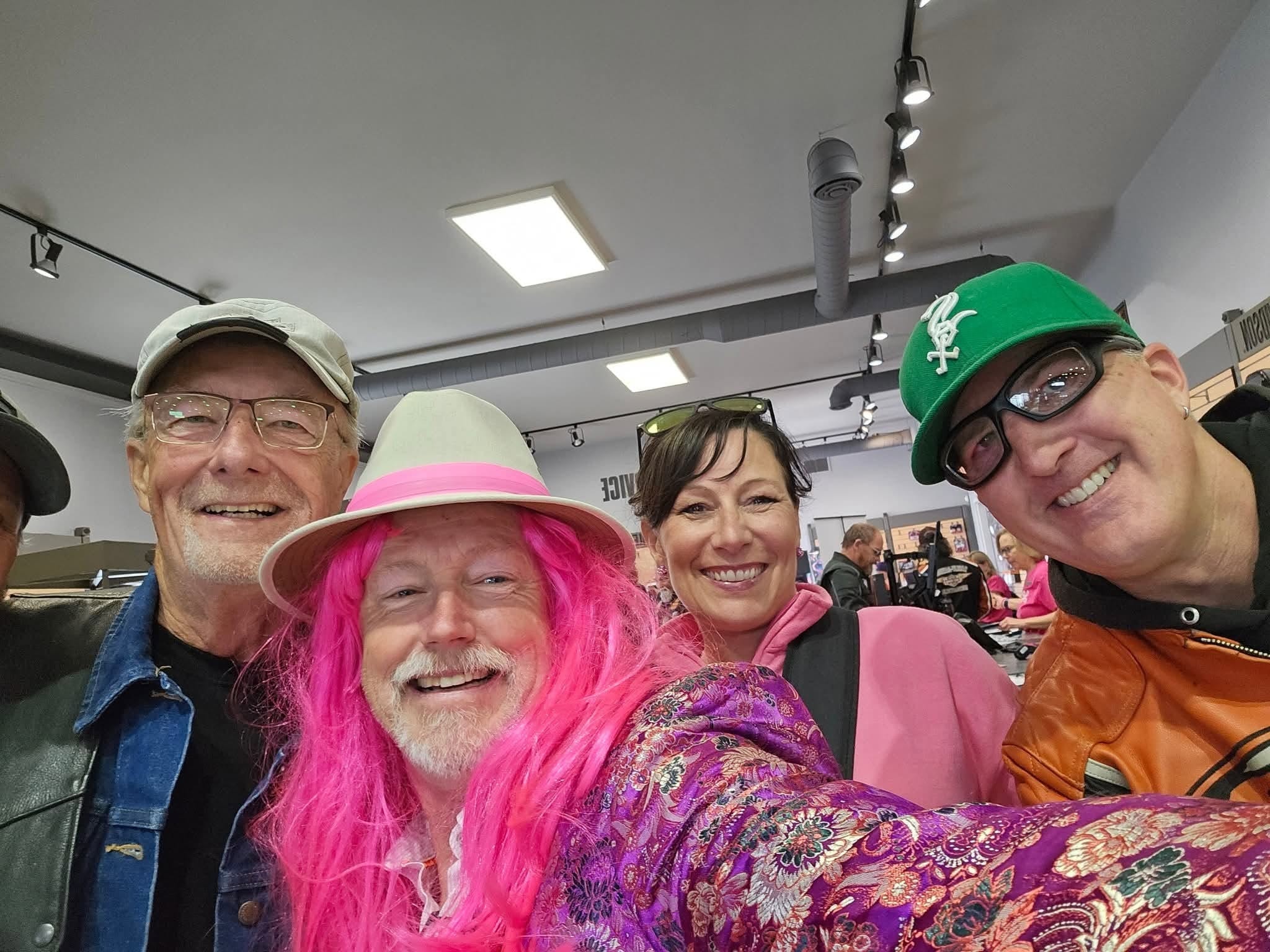 Four people inside Prairie Harley-Davidson showroom smiling for a selfie, one wearing a bright pink wig and colourful kimono at the 2025 Breast Cancer Awareness Ride