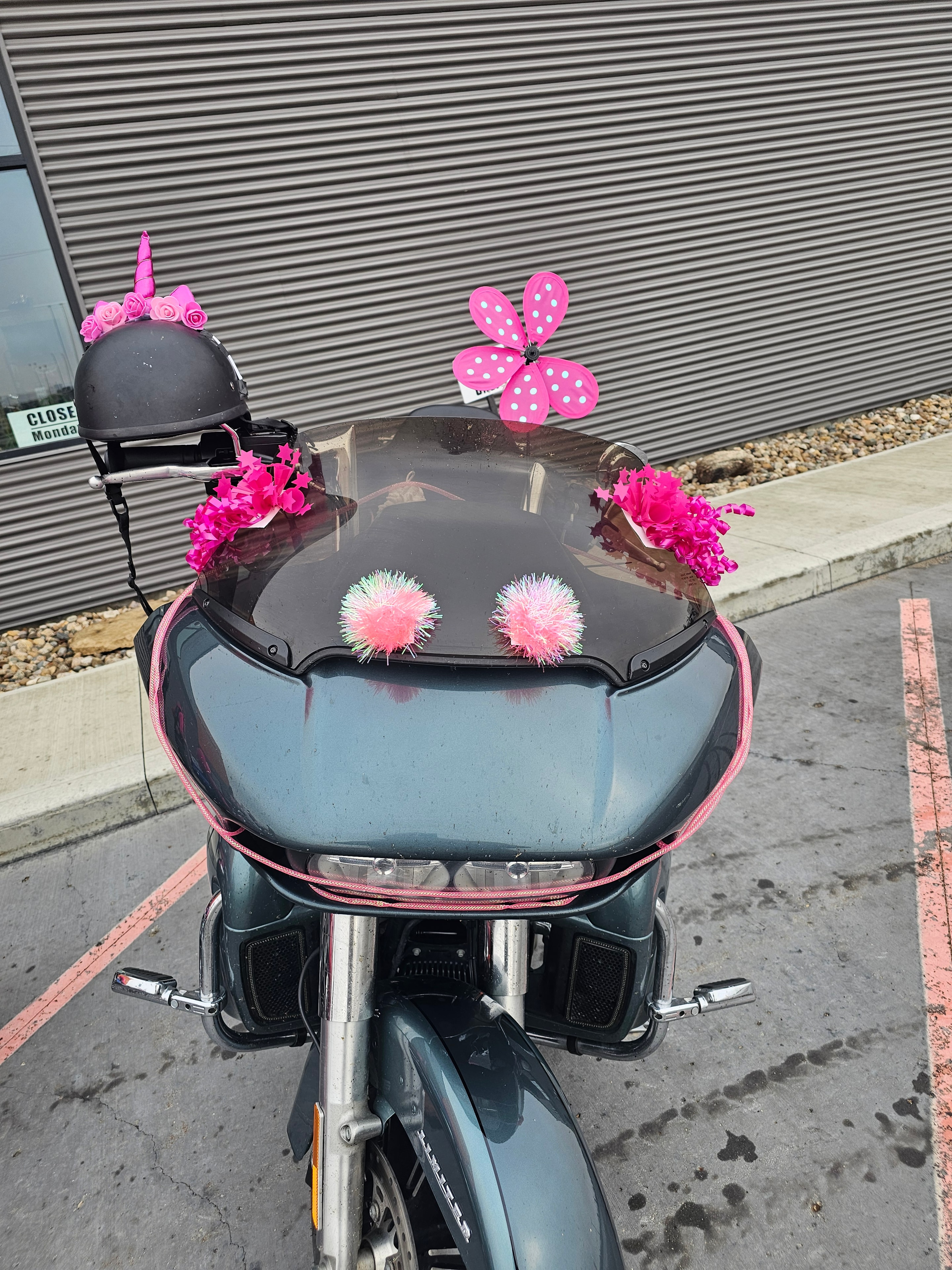 Close-up overhead view of a Harley-Davidson decorated for the 2025 Breast Cancer Awareness Ride — pink polka-dot butterfly, hot pink flowers, and fluffy pink pompoms on the windshield and helmet