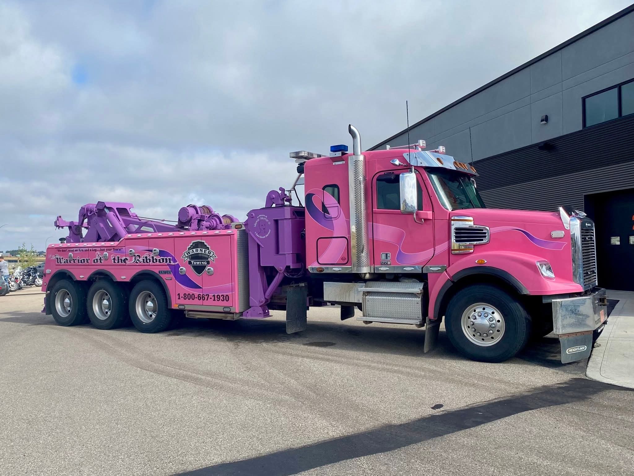 The Warner Towing 'Warrior of the Ribbon' pink-and-purple heavy-duty tow truck parked beside Prairie Harley-Davidson at the 2025 Breast Cancer Awareness Ride