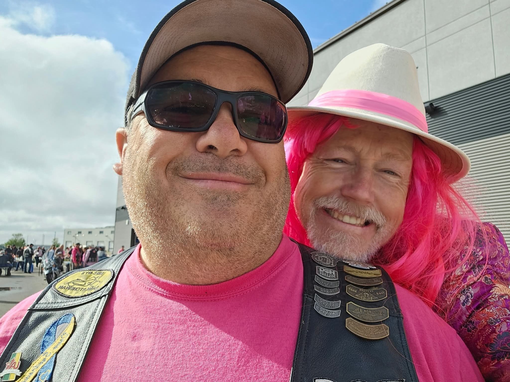Two chapter members grinning at the 2025 Breast Cancer Awareness Ride — one in a pink HOG vest, one in a bright pink wig and white fedora with a floral kimono
