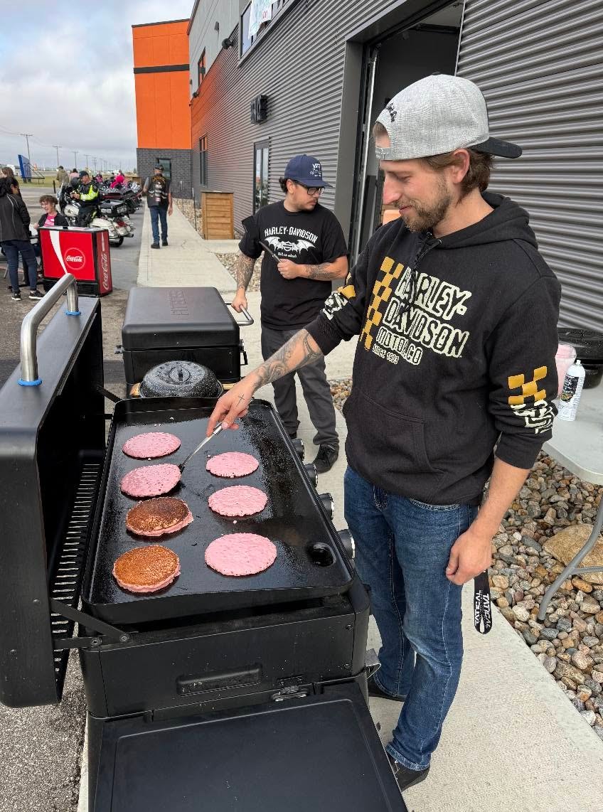 Prairie Harley-Davidson staff member in an HD hoodie flipping pink pancakes on a large outdoor griddle at the 2025 Breast Cancer Awareness Ride breakfast