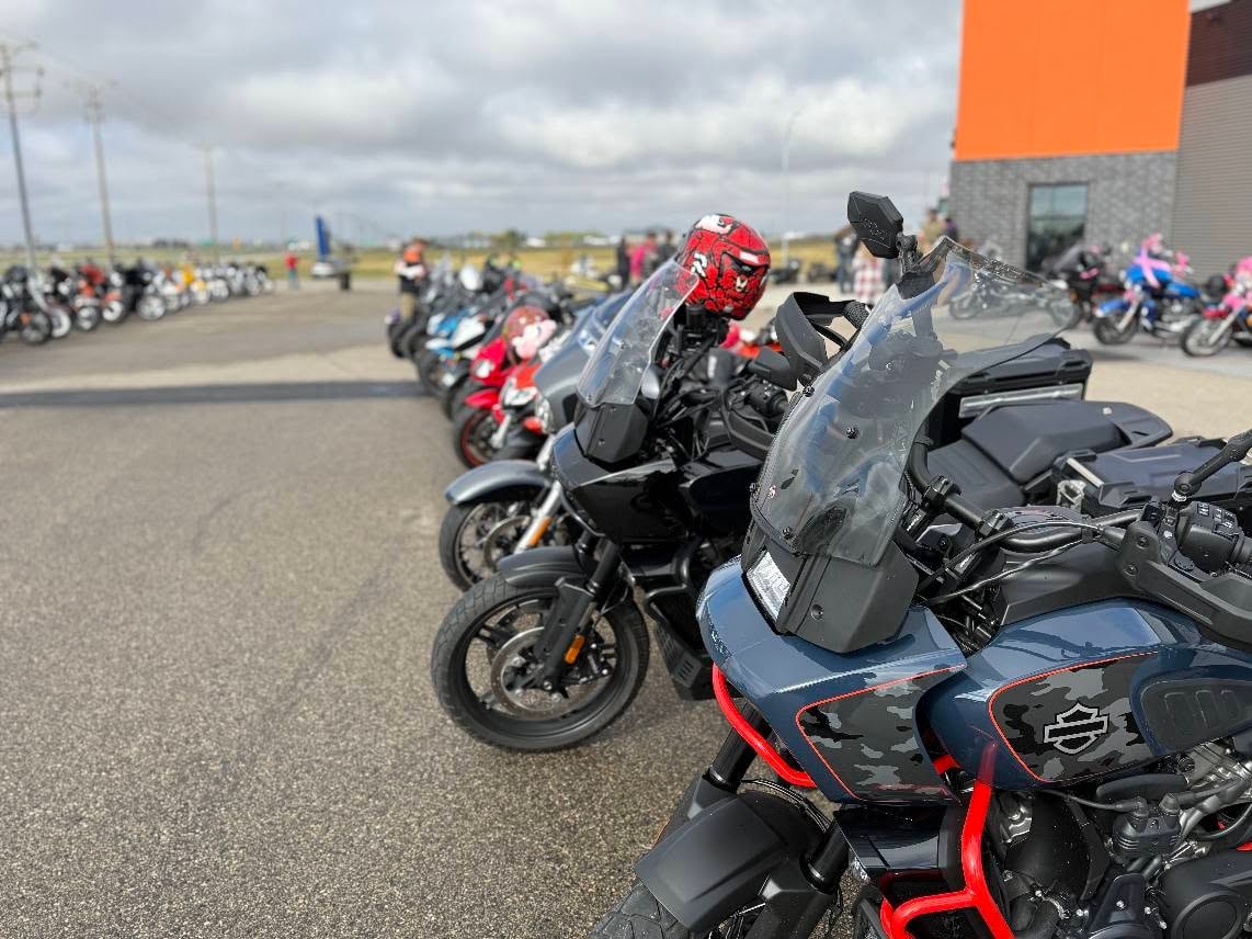 Row of bikes lined up in the Prairie Harley-Davidson parking lot under a cloudy sky, including a camo-wrapped Harley-Davidson in the foreground, at the 2025 Breast Cancer Awareness Ride